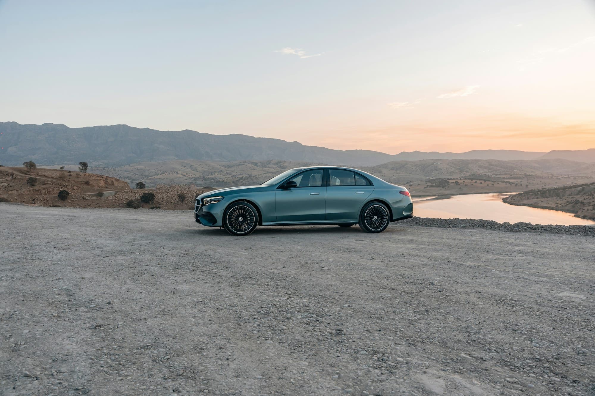 Mercedes-Benz Classe E devant un lac et des montagnes au coucher du soleil, photo provisoire
